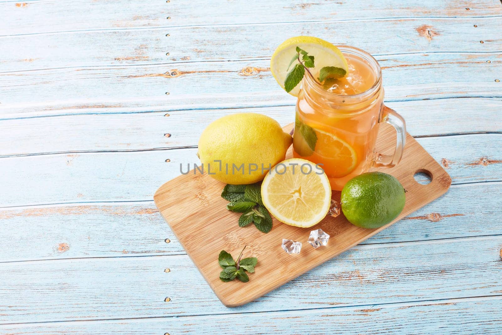 Citrus lemonade with ice, leaves of mint, lemon and lime slices standing on blue wooden table. Homemade lemonade with citruses. Healthy cool beverage