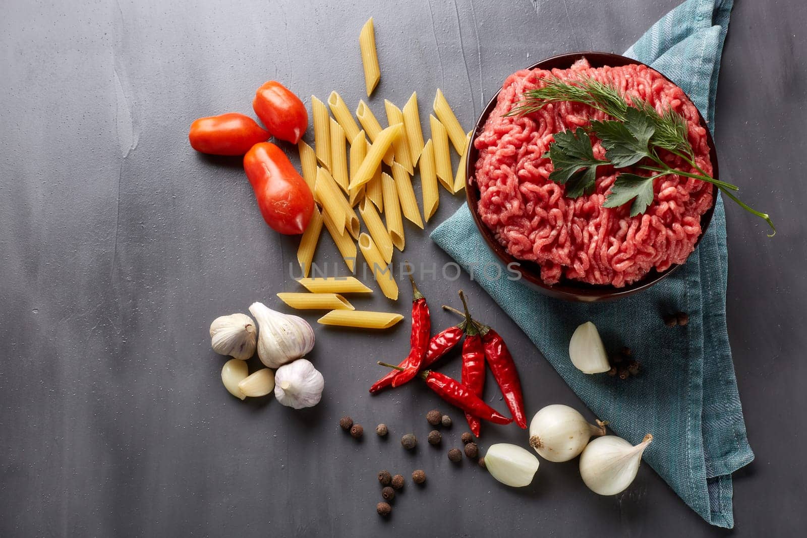 Still life with fresh forcemeat from beef in a bowl, vegetables, pasta and spices on a dark background. Top view