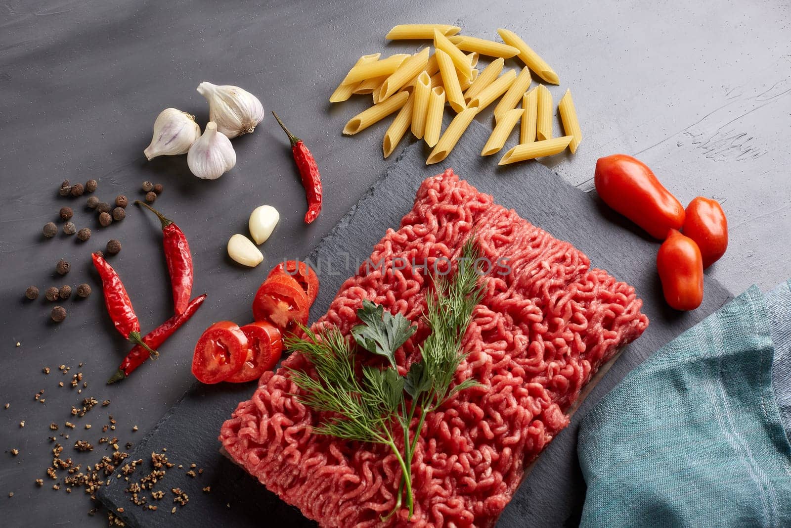 Still life with fresh forcemeat from beef, vegetables, pasta and spices on a dark background. Top view