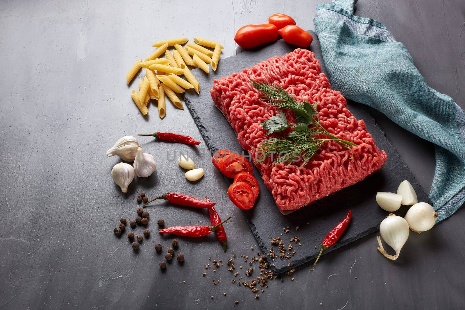 Still life with fresh forcemeat from beef, vegetables, pasta and spices on a dark background. Top view