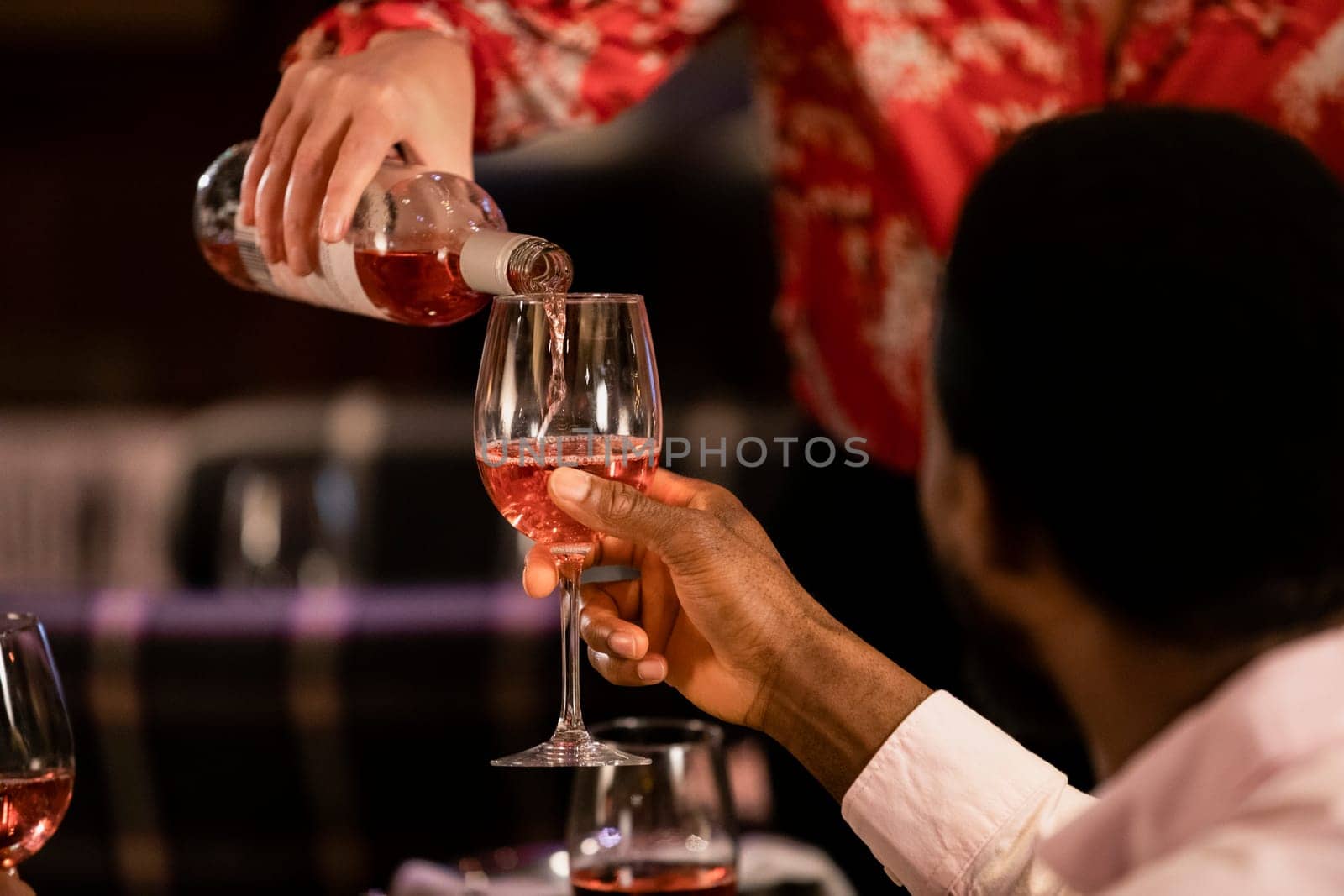 Close-up of an unrecognisable person holding a wine glass up as a waiterss fills it up with rose wine.