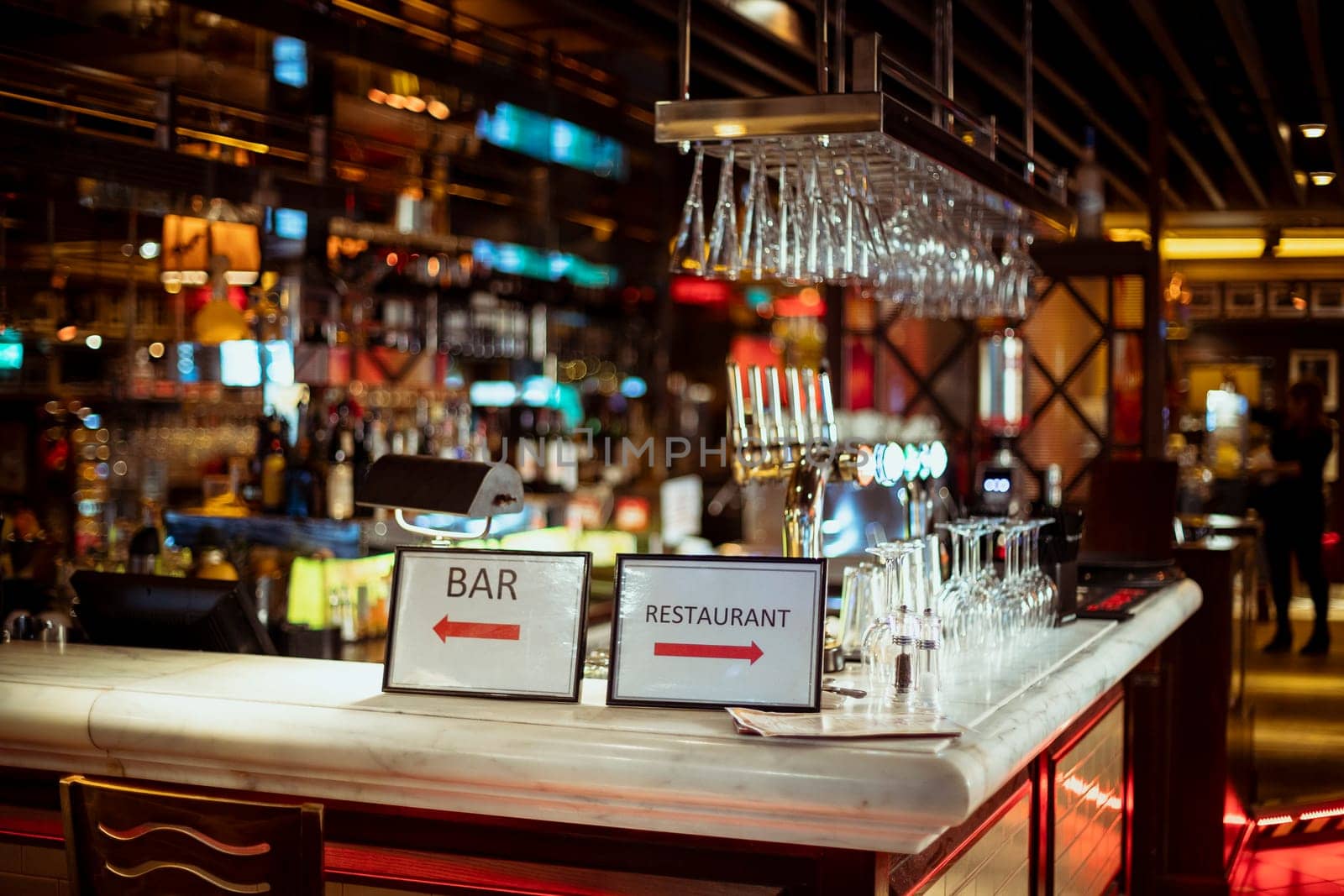 Interior shot of a restaurant bar counter which has signs pointing to either the bar or the restaurant.