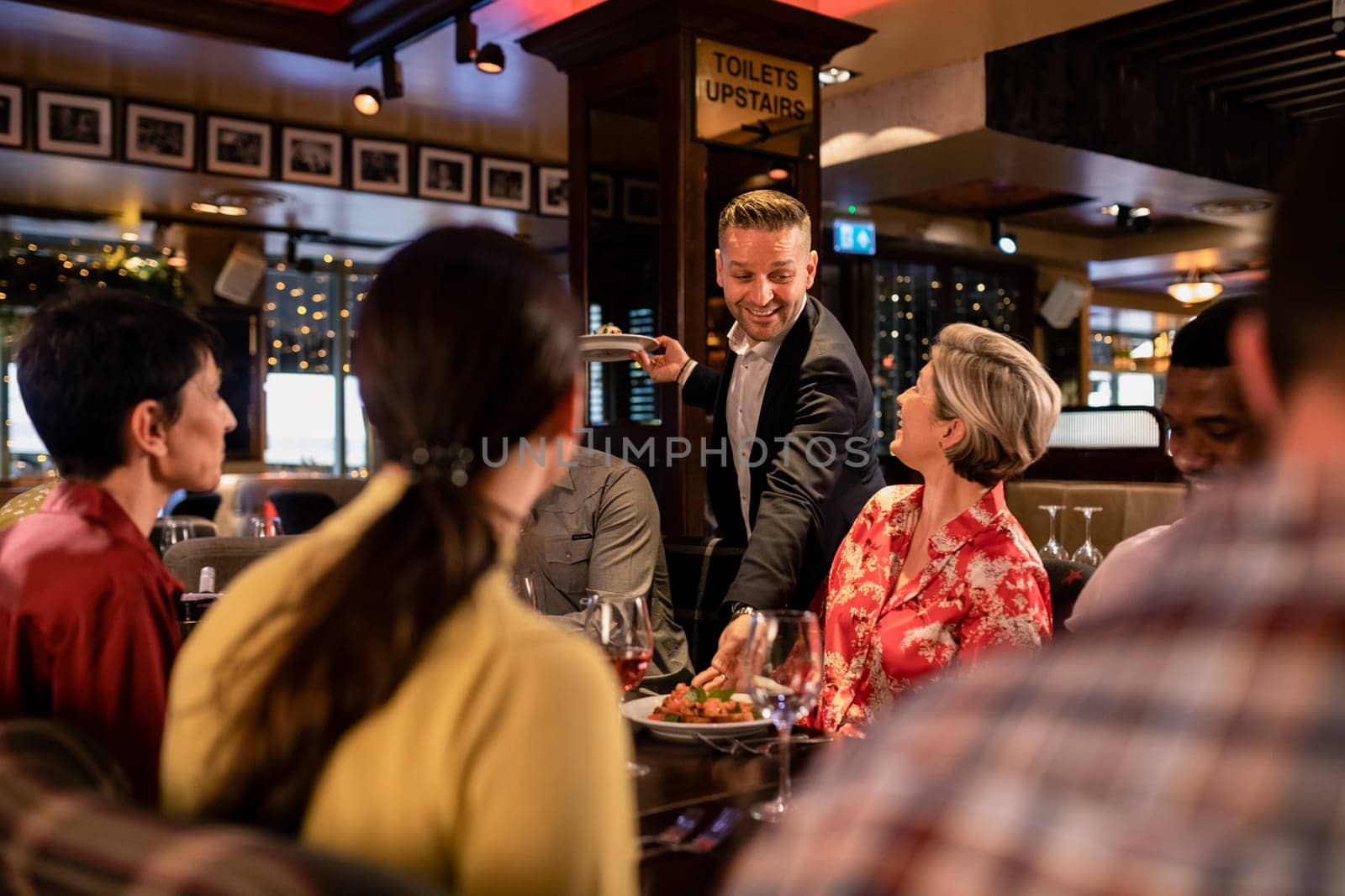 Male waiter placing food down on a table where a small group of friends are sitting together.