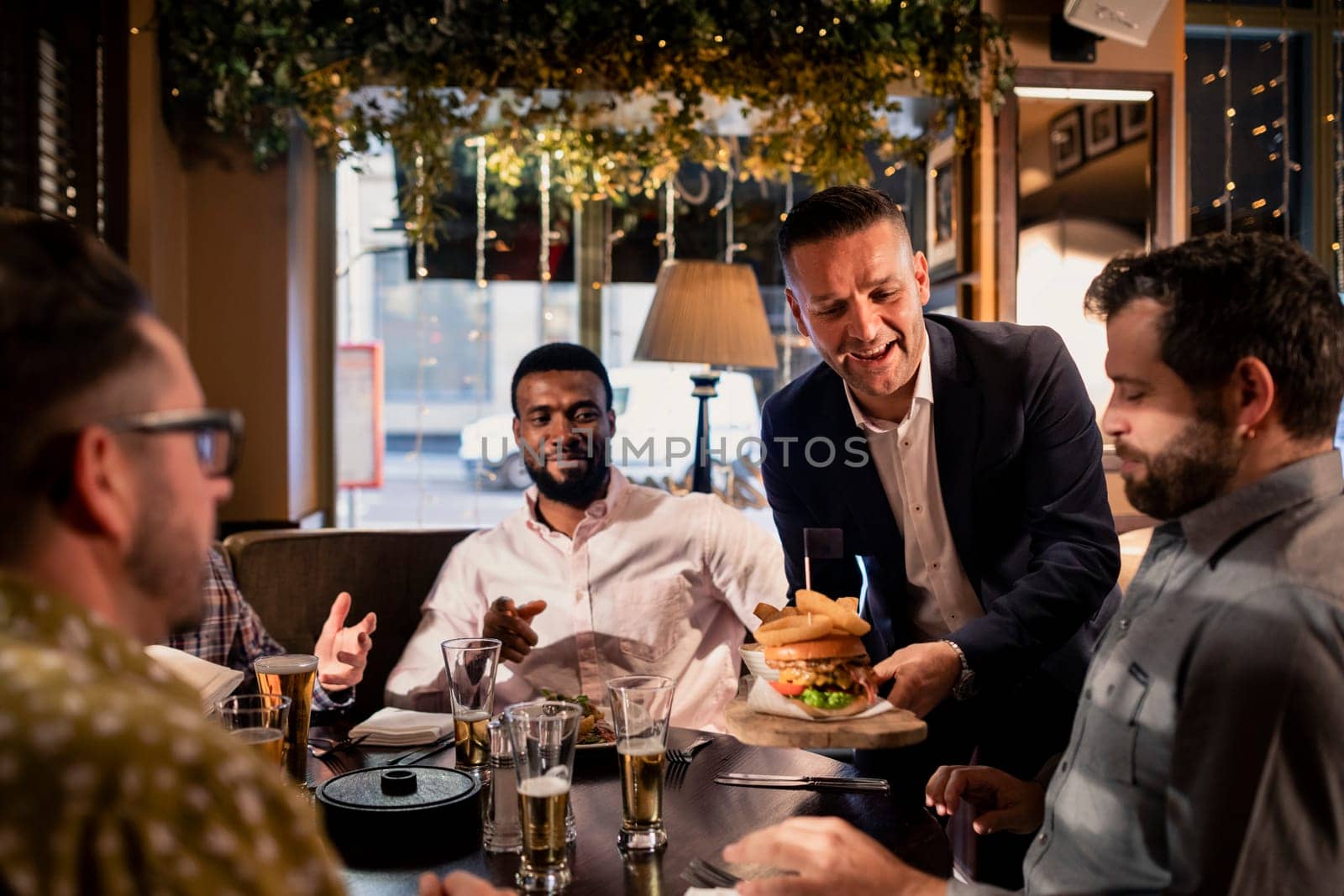 Mid adult waiter placing a meal down on the table where a small group of mid adult men are sitting and relaxing.