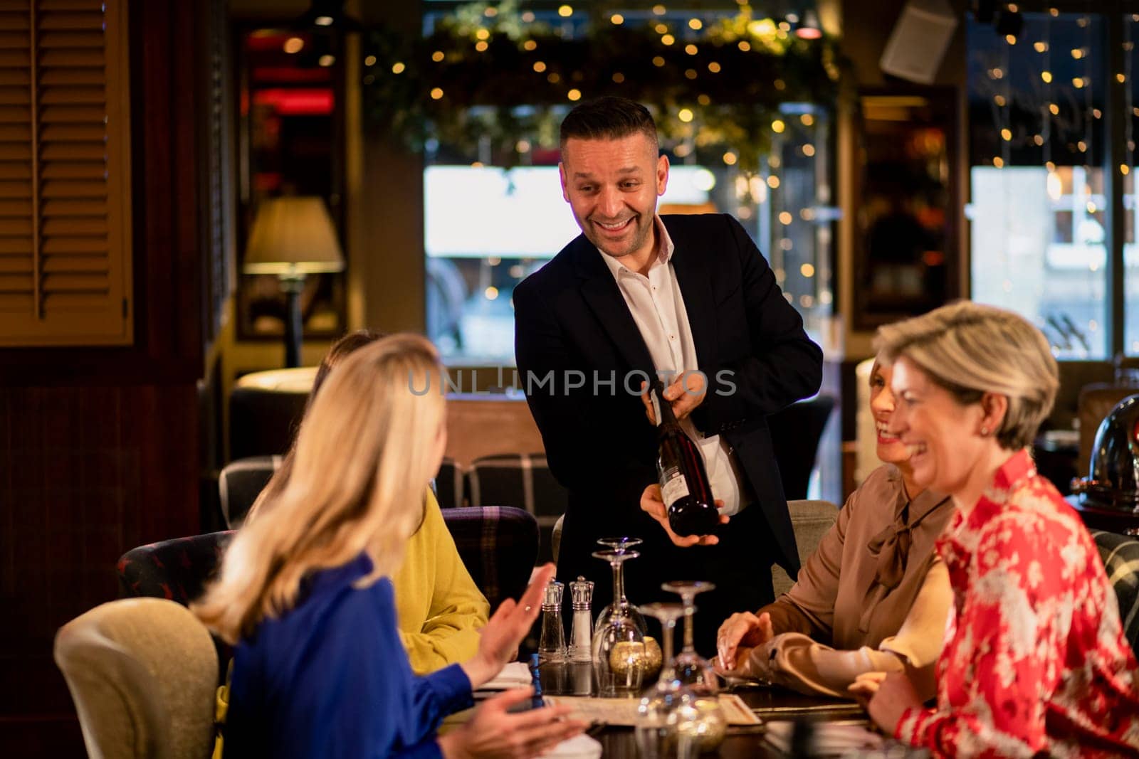 Mature waiter reccomending a bottle of champagne to a small group of mature women. They are sitting at a table in a restaurant.