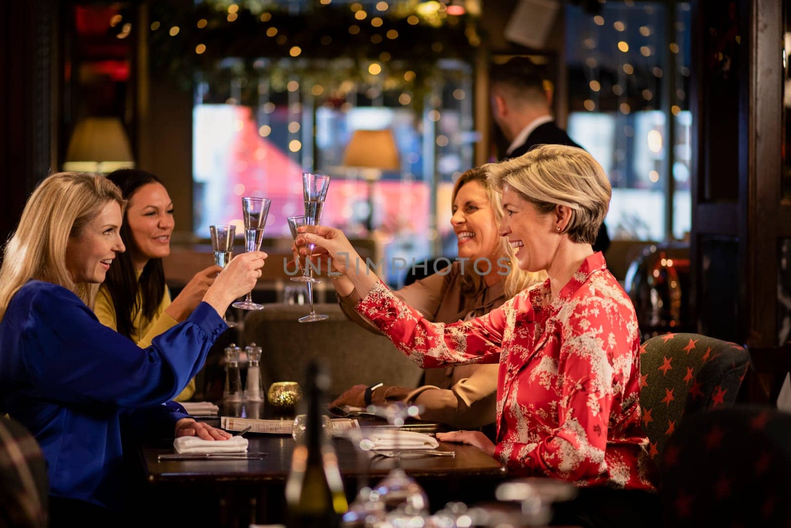 Small group of mature female friends making a celebratory toast while sitting around a table in a restaurant.