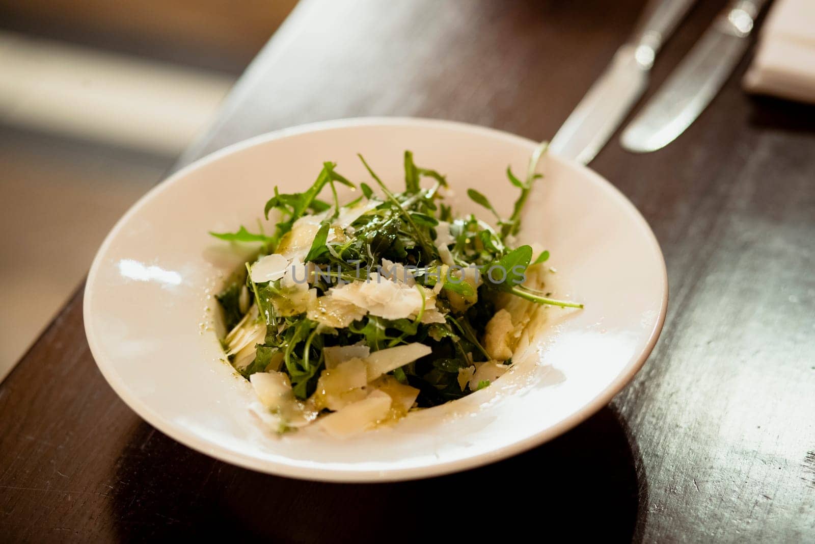 Restaurant style parmesan and rocket salad presented in a bowl on a wooden table in a restaurant.
