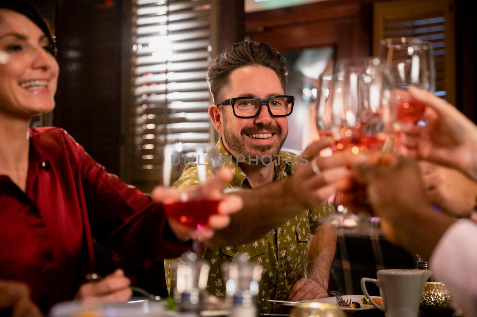 Cheerful mature man raising his glass for a celebratory toast with her friends while sitting in a restaurant having a meal.