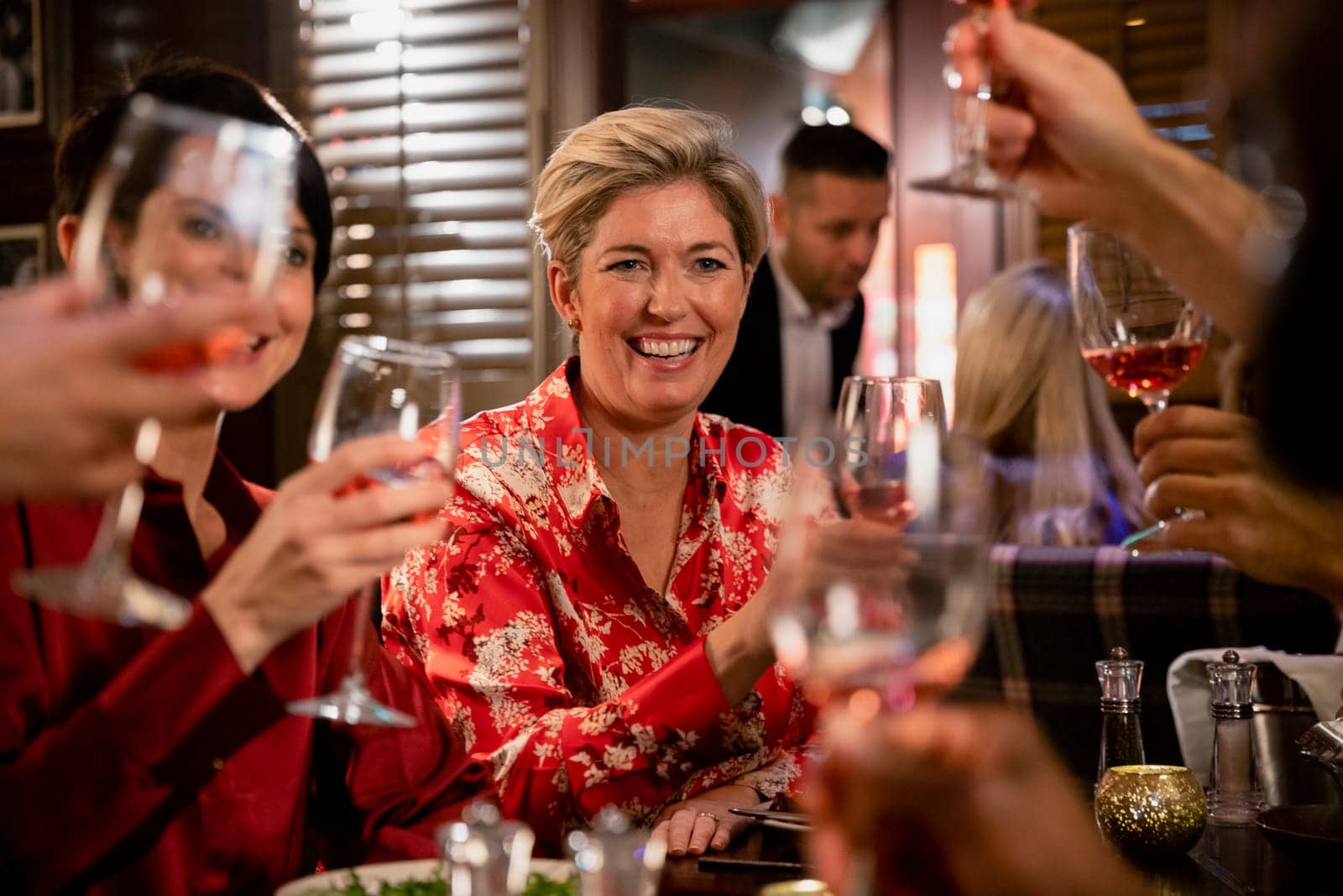 Cheerful mature woman raising her glass for a celebratory toast with her friends while sitting in a restaurant having a meal.