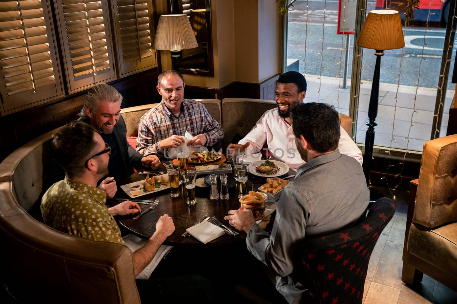 Group of mature men sitting at the table in a restaurant. They are enjoying food, talking and laughing.