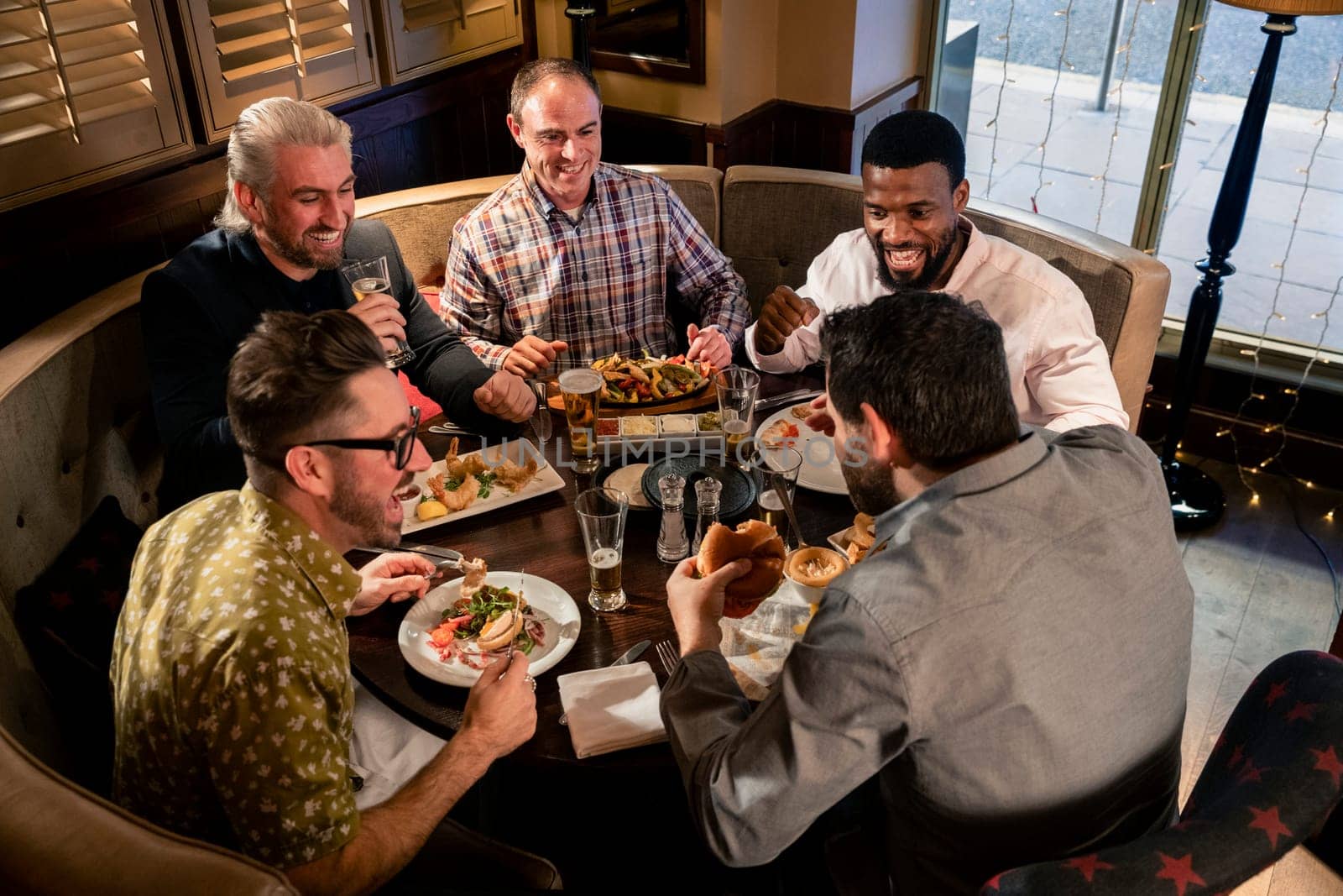 Group of mature men sitting at the table in a restaurant. They are enjoying food, talking and laughing.