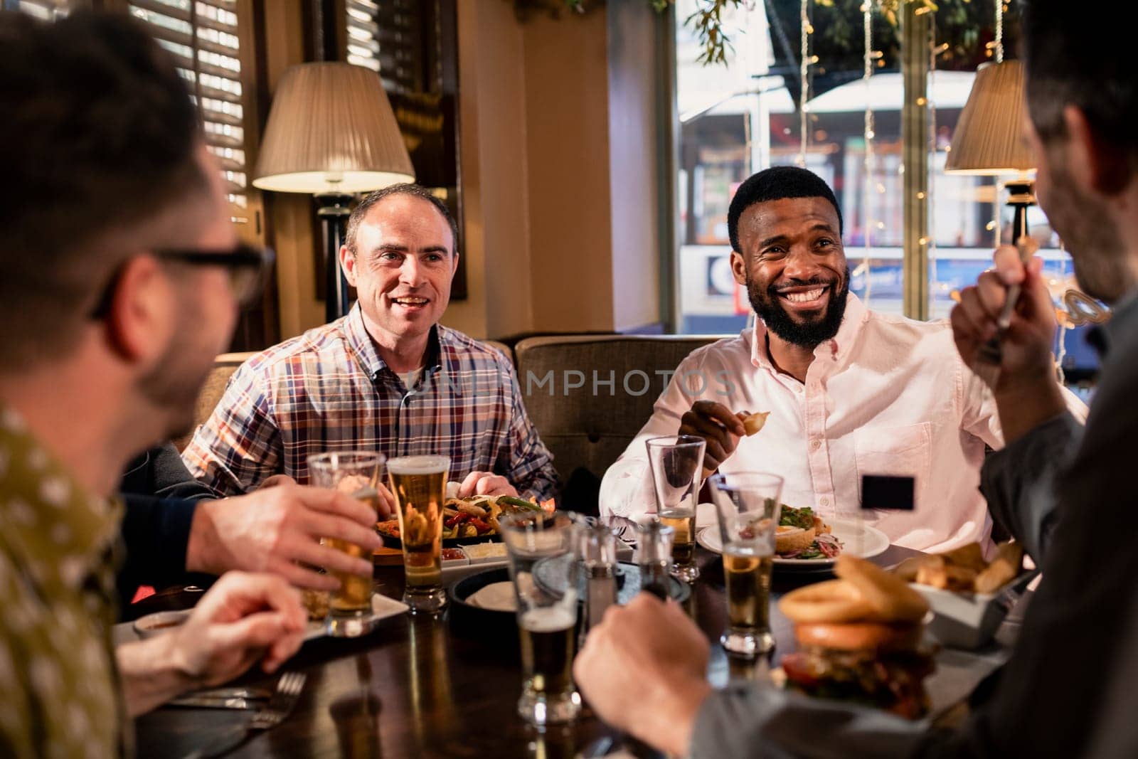 Small group of mid adult male friends enjoying some food in a restaurant. They are talking and enjoying each others company.