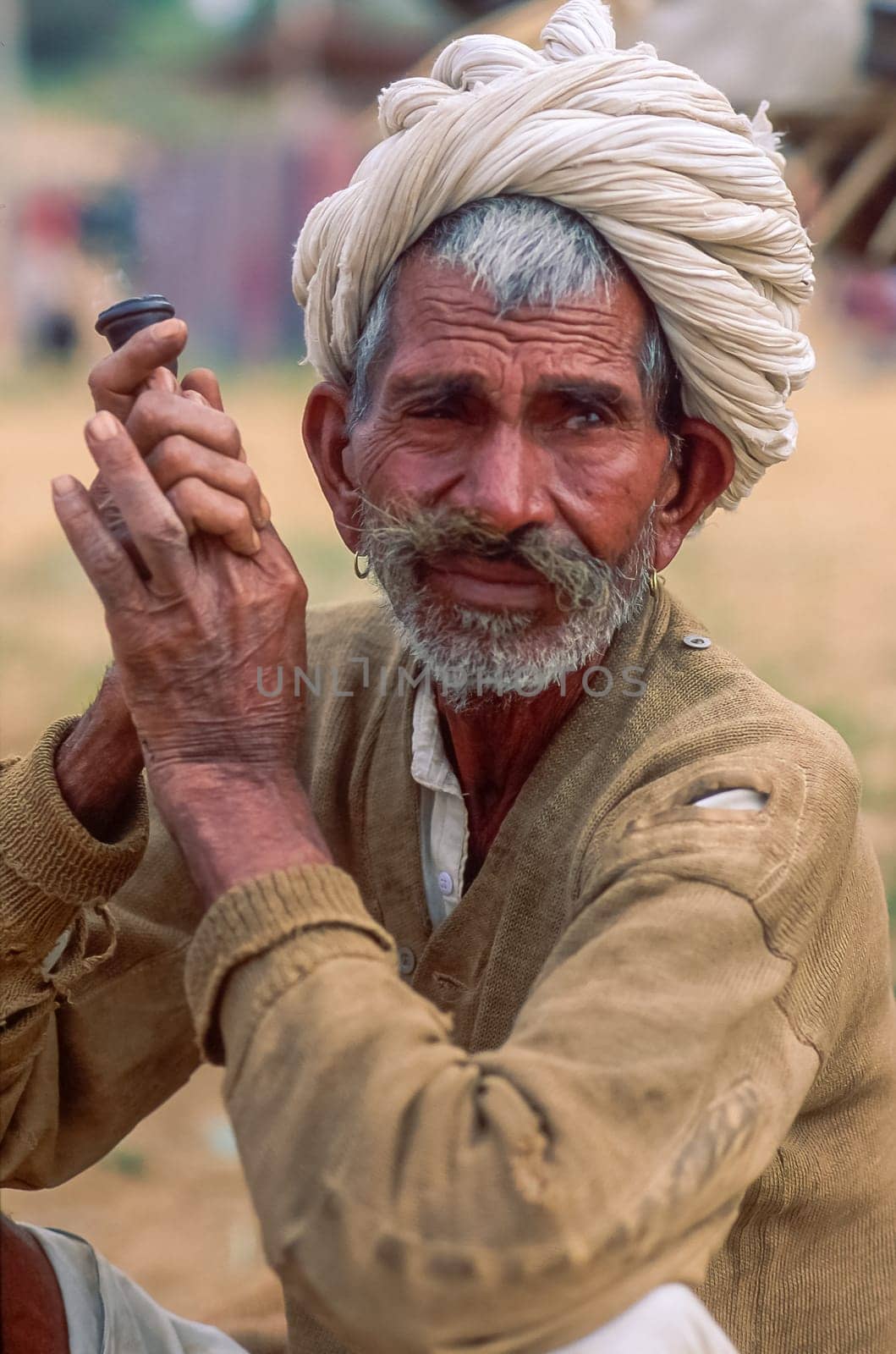 Portrait of an elderly indian man staring sideways while holding a chillum, white turban and traditional clothes. Shot at the Pushkar Camel Fair, Rajasthan, India.