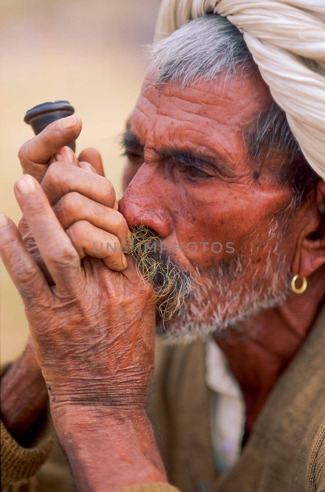 Close-up of a rajasthani senior man smoking a pipe, wearing an earring and a white turban, Camel Fair at Pushkar, Rajasthan, India