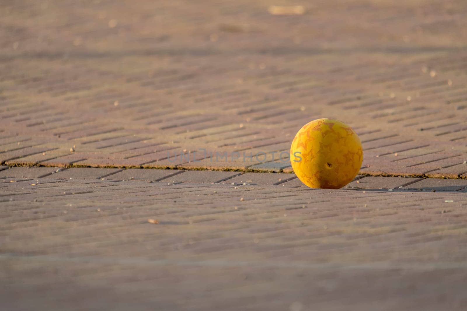 Yellow Kids Ball Lies on a Paved Place in front of Blurred Background