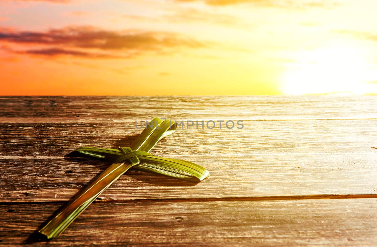 Cross shape of palm leaf on wooden table with rays of sunset background. Palm Sunday concept