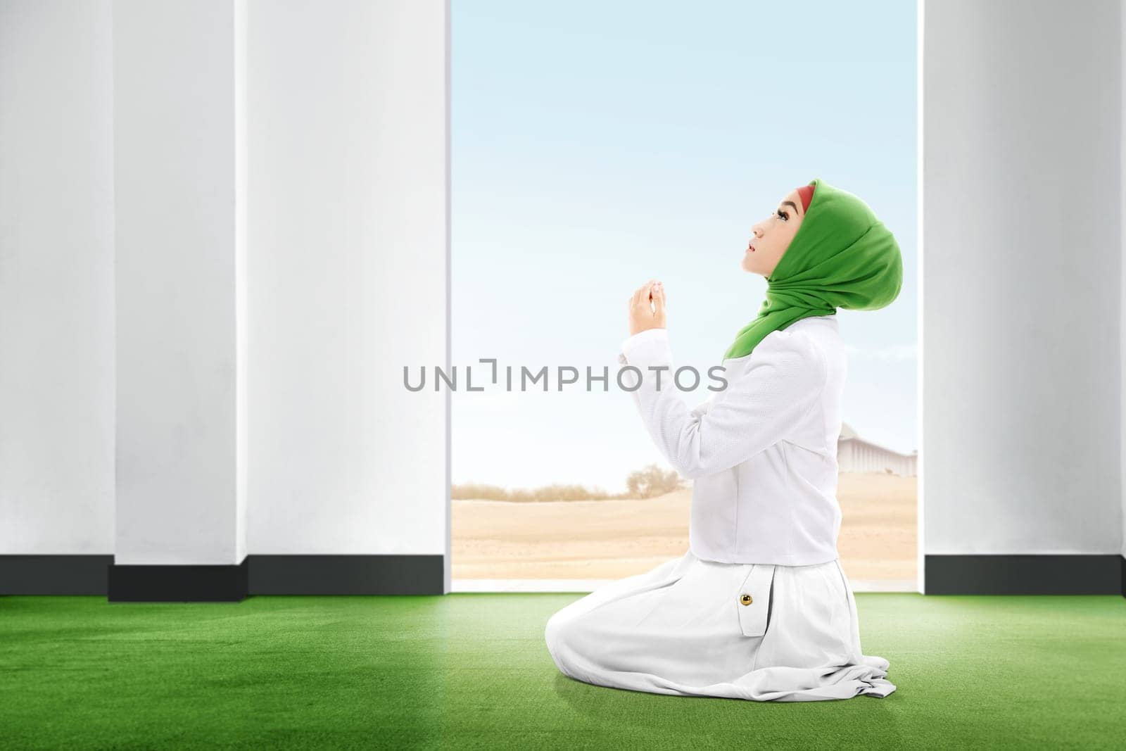 Pretty asian woman in veil sitting in praying position on the carpet rise the hands and looking up inside the room with open door and blue sky background