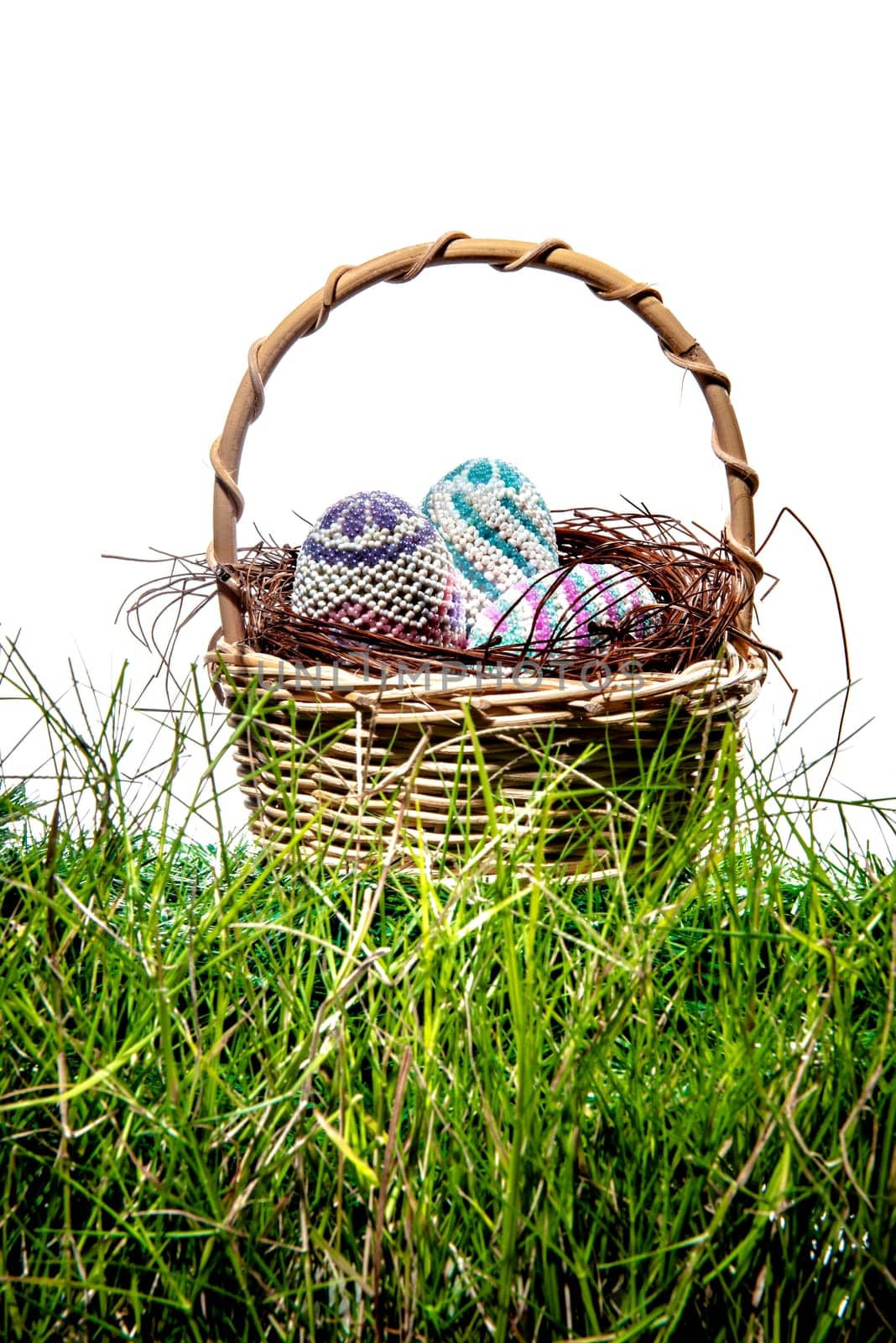 Colorful easter eggs in the nest on wooden basket at green grass over white background. Happy Easter