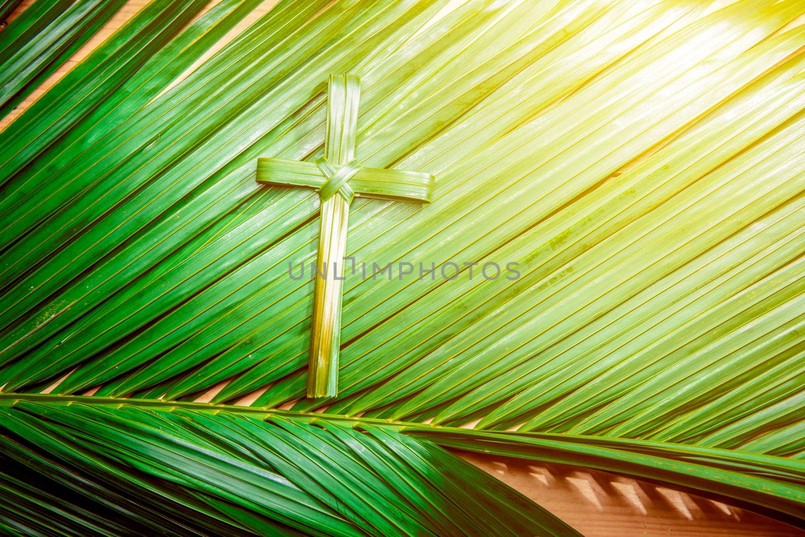 Cross shape of palm leaf on palm branches with ray in wooden background. Palm Sunday concept