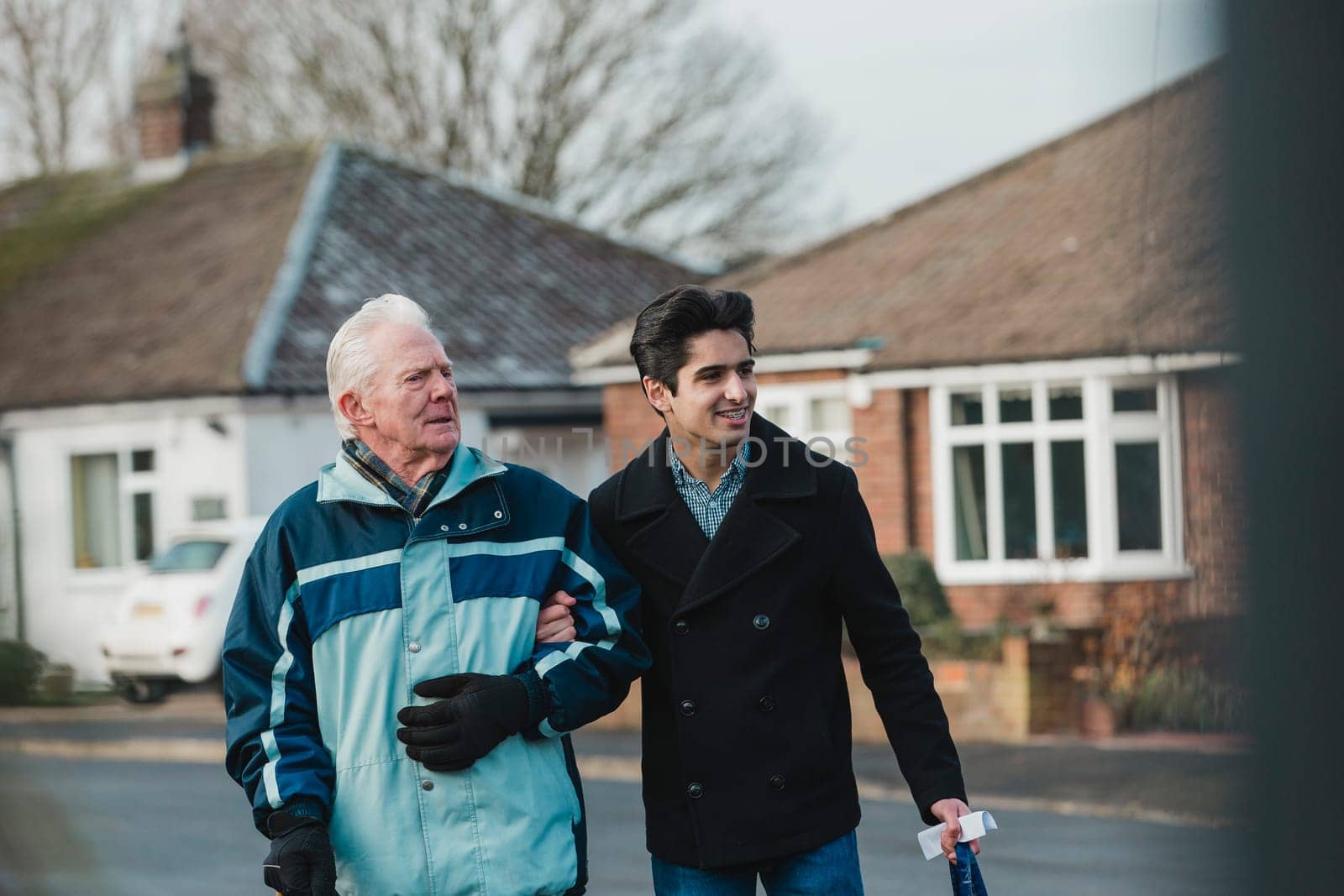 Teenage boy is walking back from the shop with his grandparent. He is carrying the shopping bag and they are linking arms.