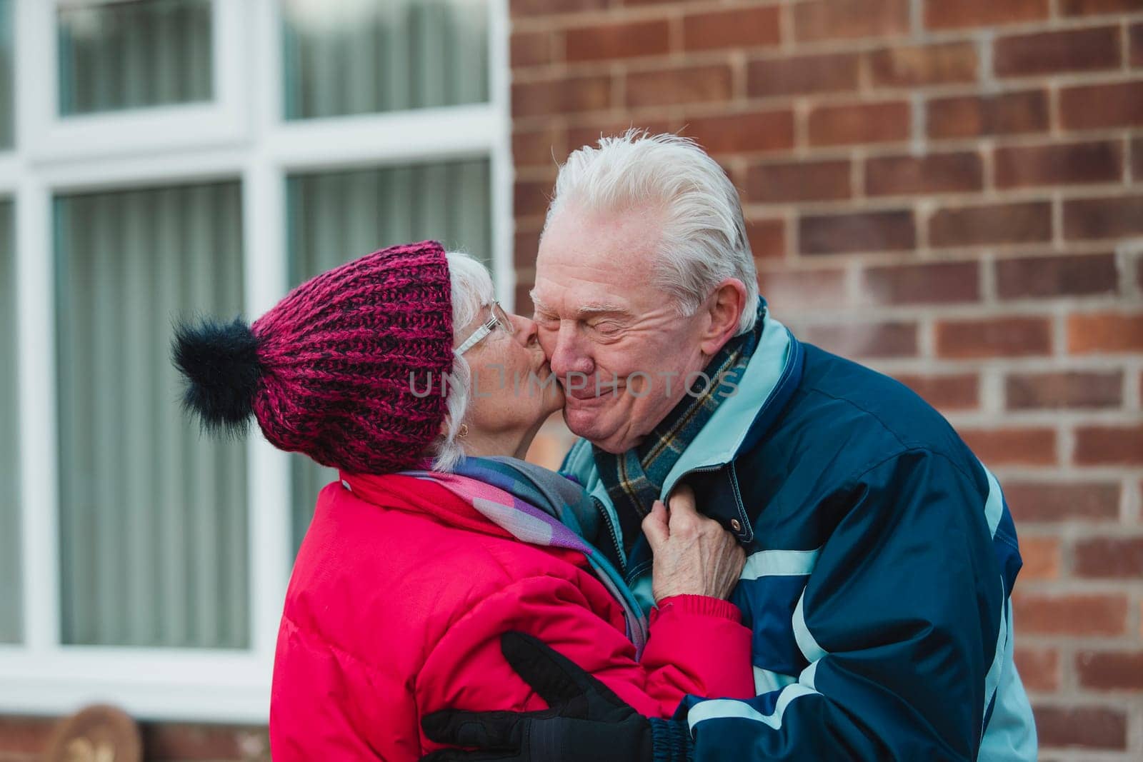 Senior woman is kissing her husband outside of their home in the winter.