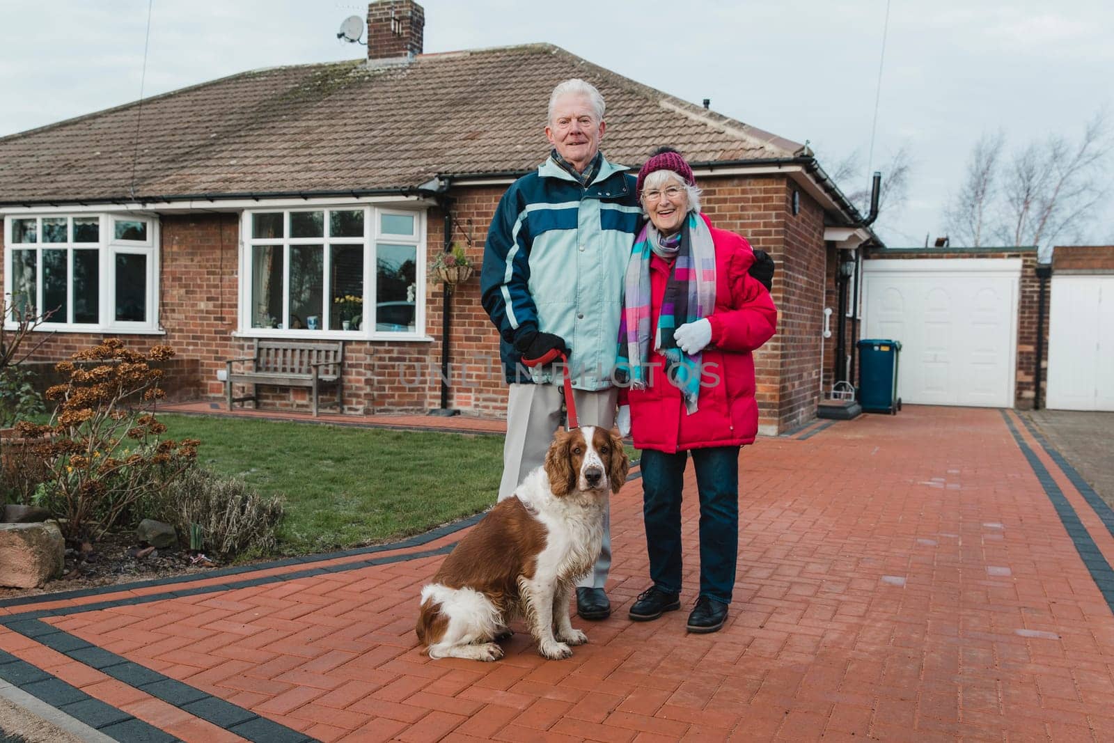 Portrait of a senior couple and their pet dog in the front yard of their house.