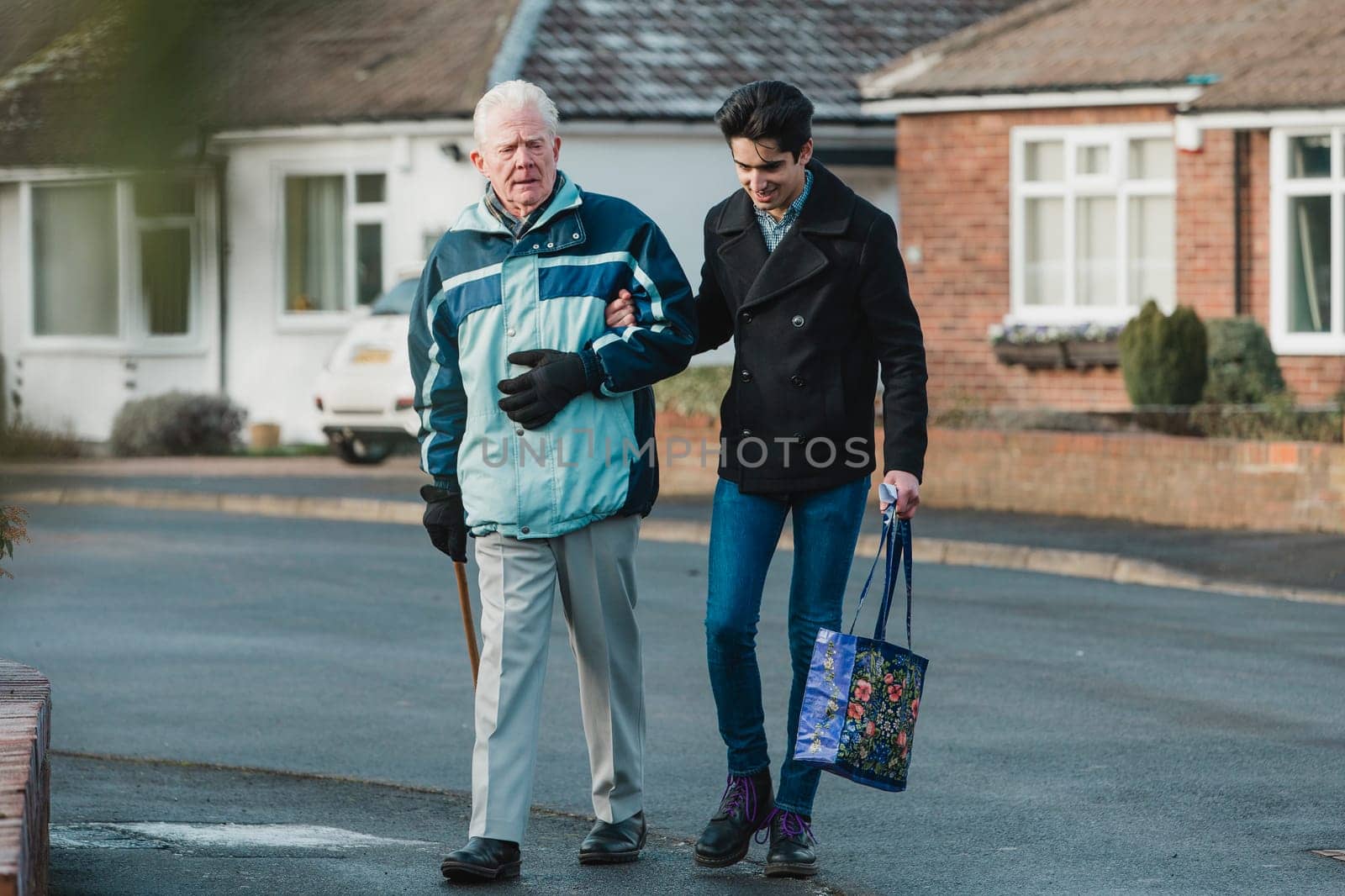 Teenage boy is walking back from the shop with his grandparent. He is carrying the shopping bag and they are linking arms.