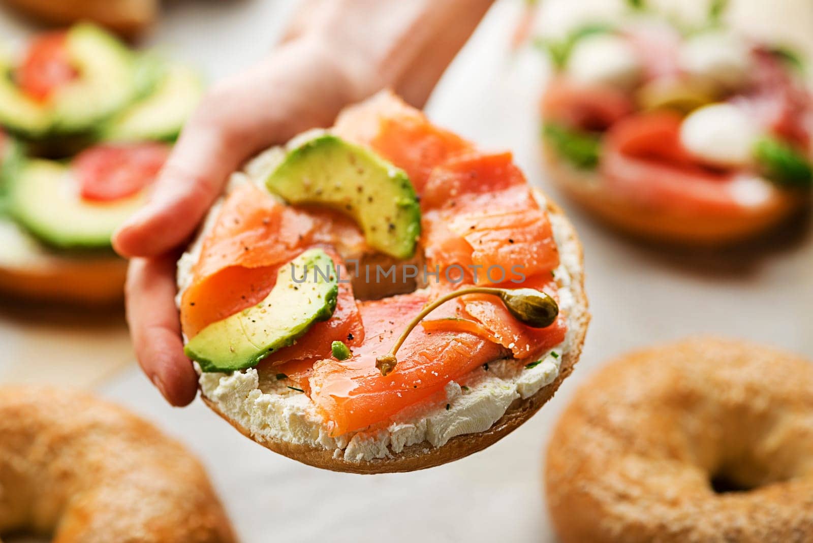 Woman is holding a Bagel with cream, avocado and smoked salmon oHealthy breakfast food.