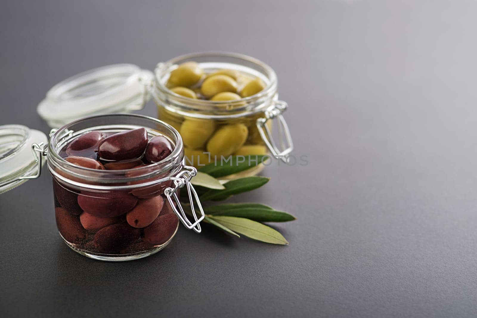 Pickled green and black olives in glass jar with branch leaves
