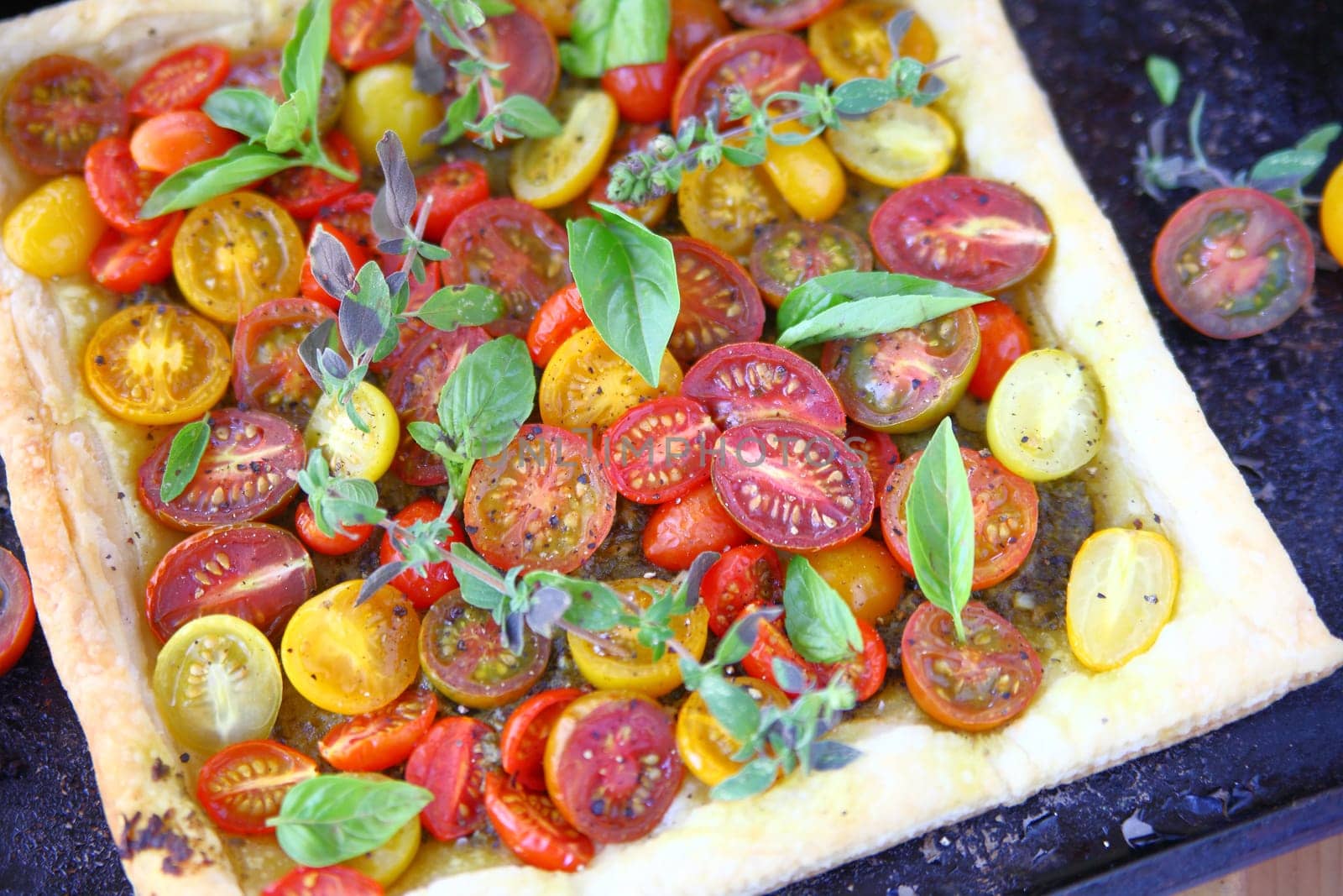 Overhead view of cherry tomato tart on puff pastry with basil and oregano leaves