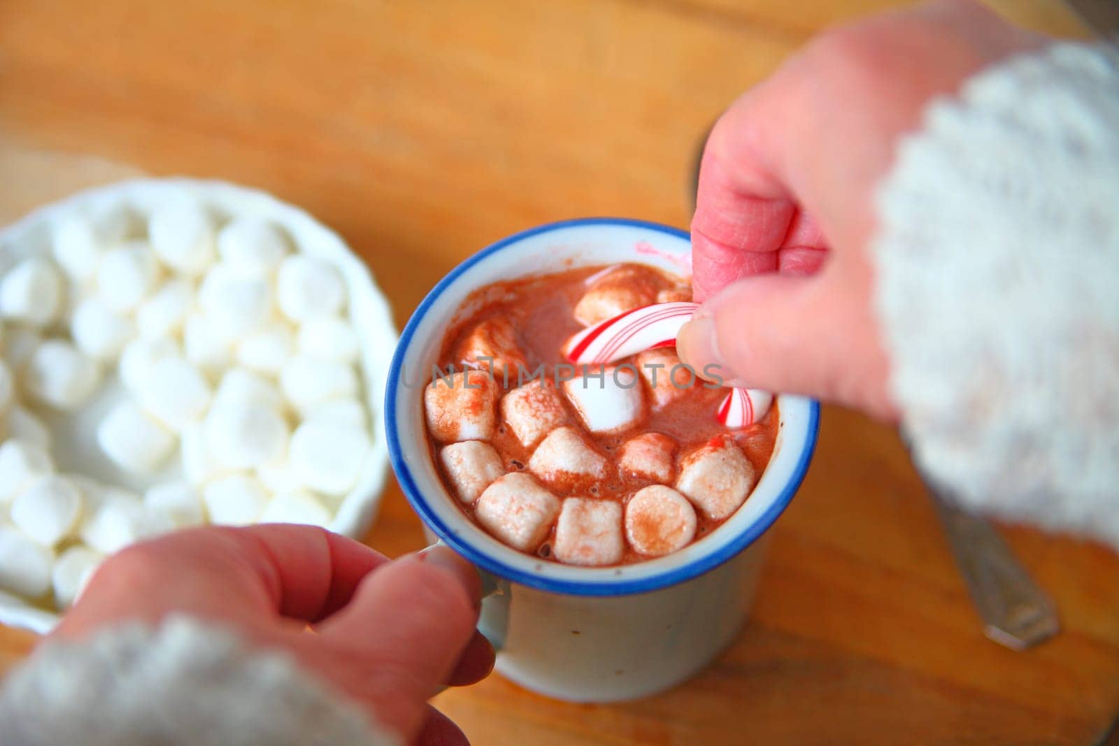 A woman holds a candy cane in a mug of hot chocolate with marshmallows