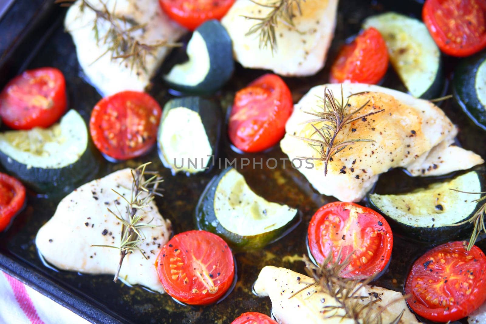 Overhead view of boneless chicken, zucchini and cherry tomatoes on baking pan