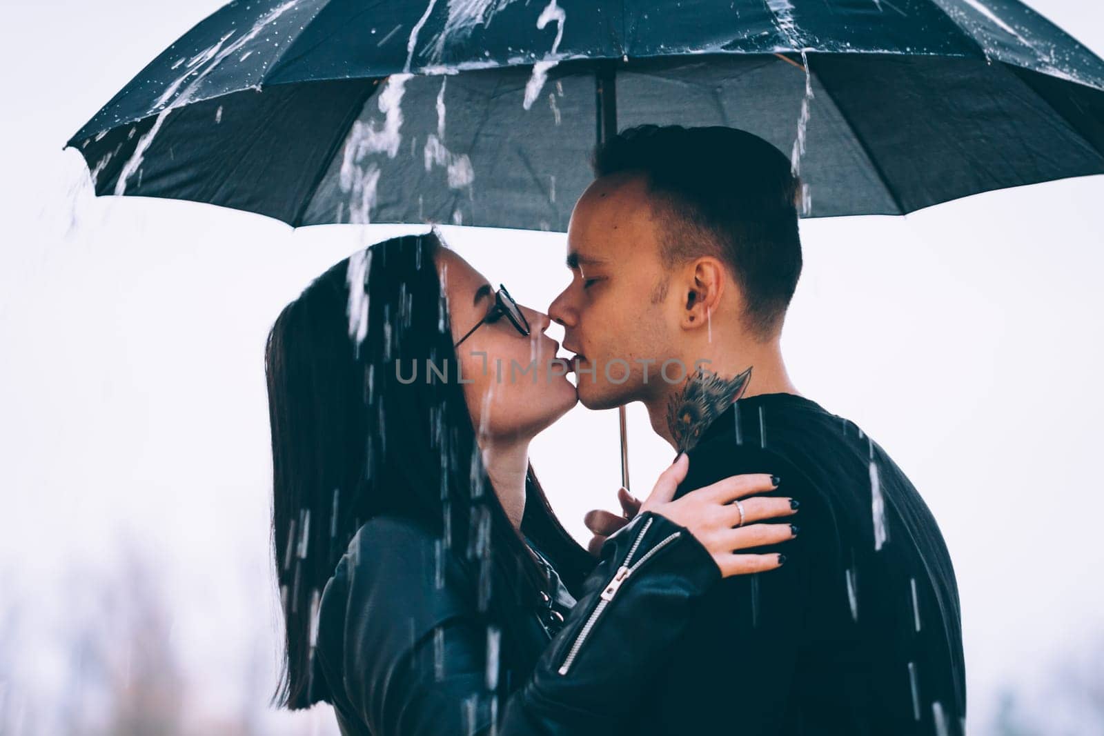young couple standing under a dark umbrella.