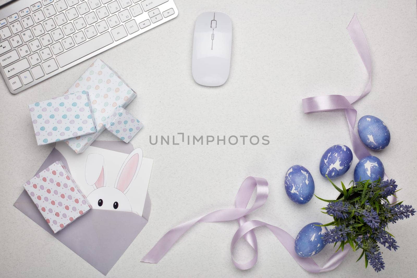 Colored easter eggs, gift box, computer keyboard and mouse, blank sheet with envelope on a lilac background. Top view with copy space. Greeting card, Easter background
