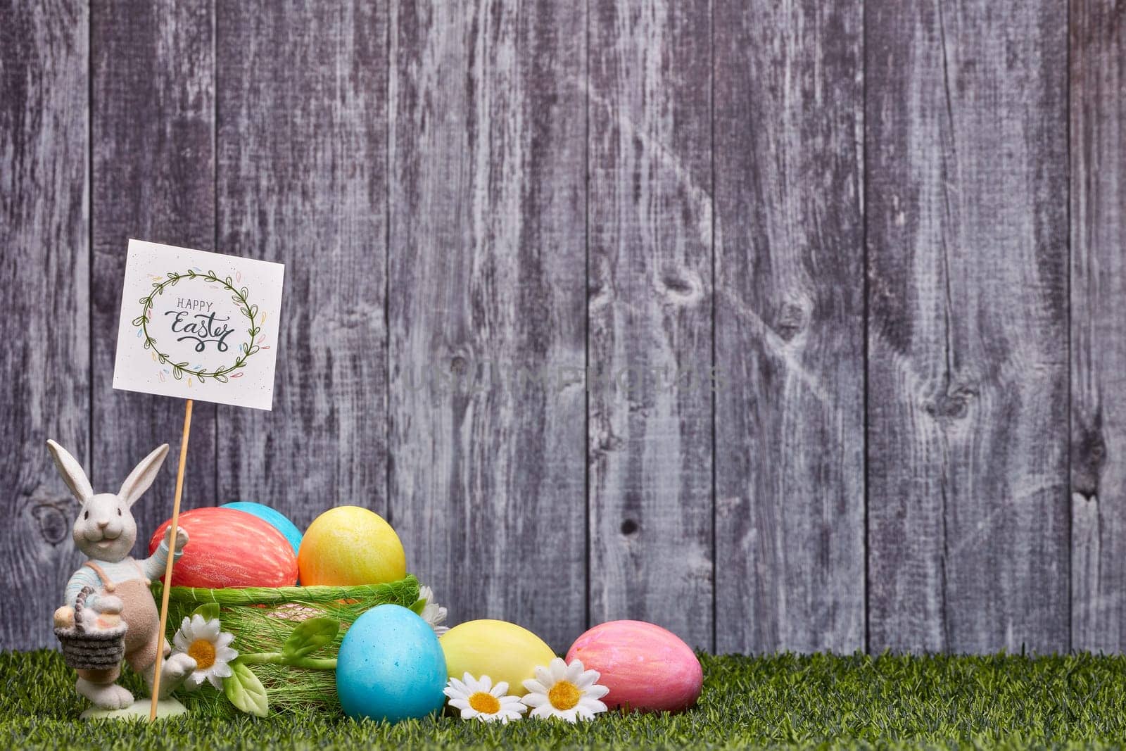 Colored easter eggs, easter rabbit and flowers lying on a green grass on a grey wooden background with copy space. Greeting card, Easter background