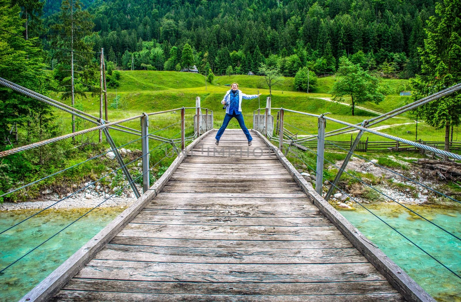 happy distant woman jump of a wooden pedestrian bridge footbridge over river Soca in Slovenia in  wild nature background .
