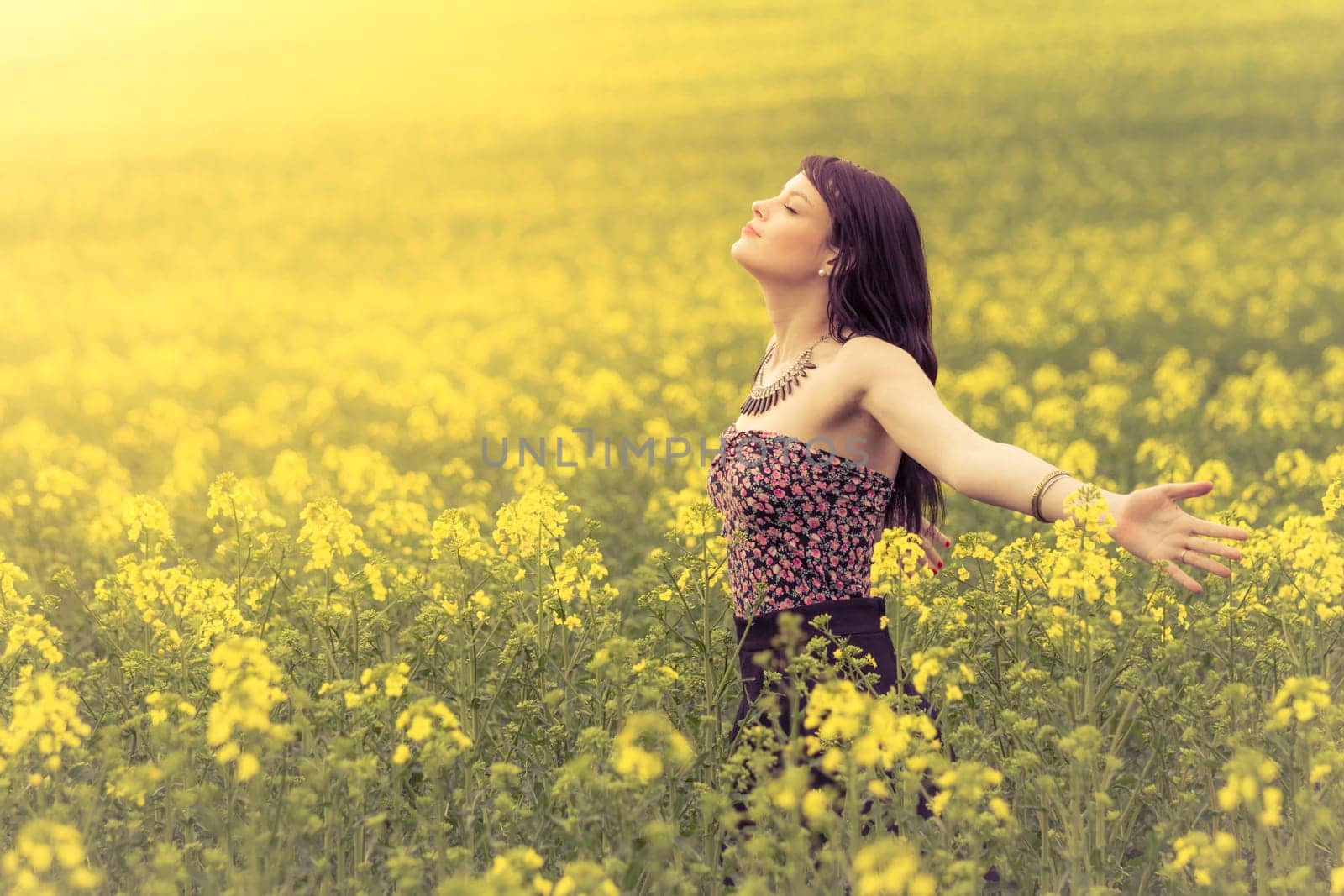 Attractive young beauty girl enjoying the warm sunny sun in nature rapeseed field takes time feeling sustainability and contemplation.