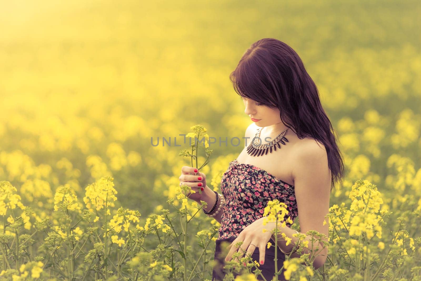 Attractive young beauty girl enjoying the warm sunny sun in nature rapeseed field takes time feeling sustainability and contemplation.