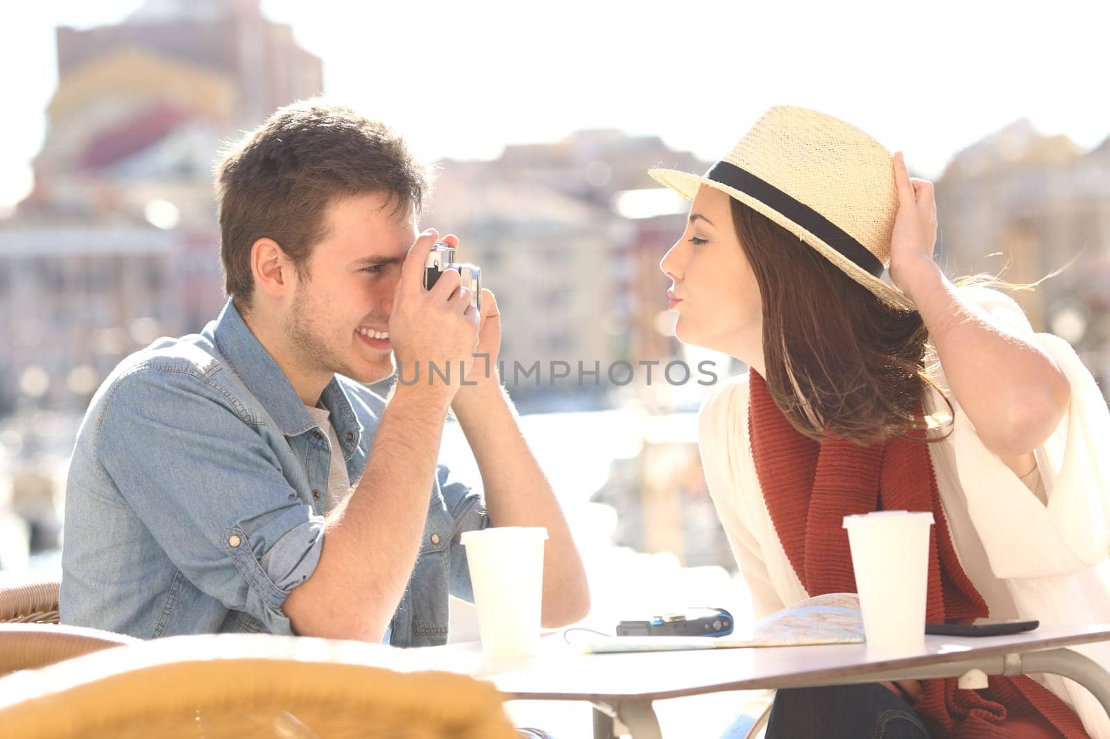Side view of a tourist joking and photographing his girlfriend in a hotel terrace during summer holidays