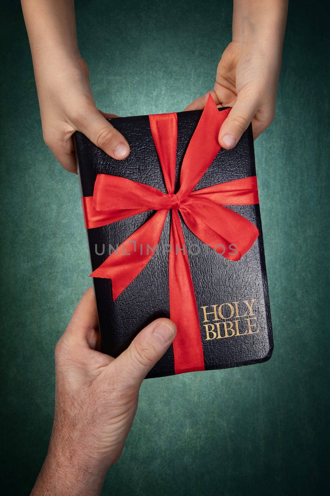 Hand of man giving to a child a Holy Bible as a gift, tied in red ribbon