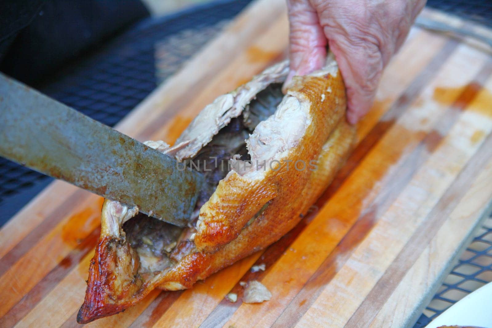 A man uses an old knife on a roast duck on a cutting board
