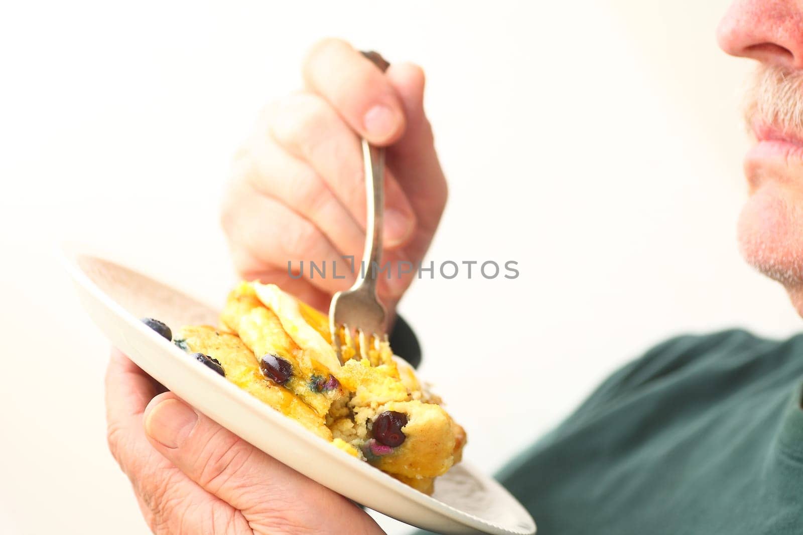 An older man holds a fork and a dish of pancakes with room for text