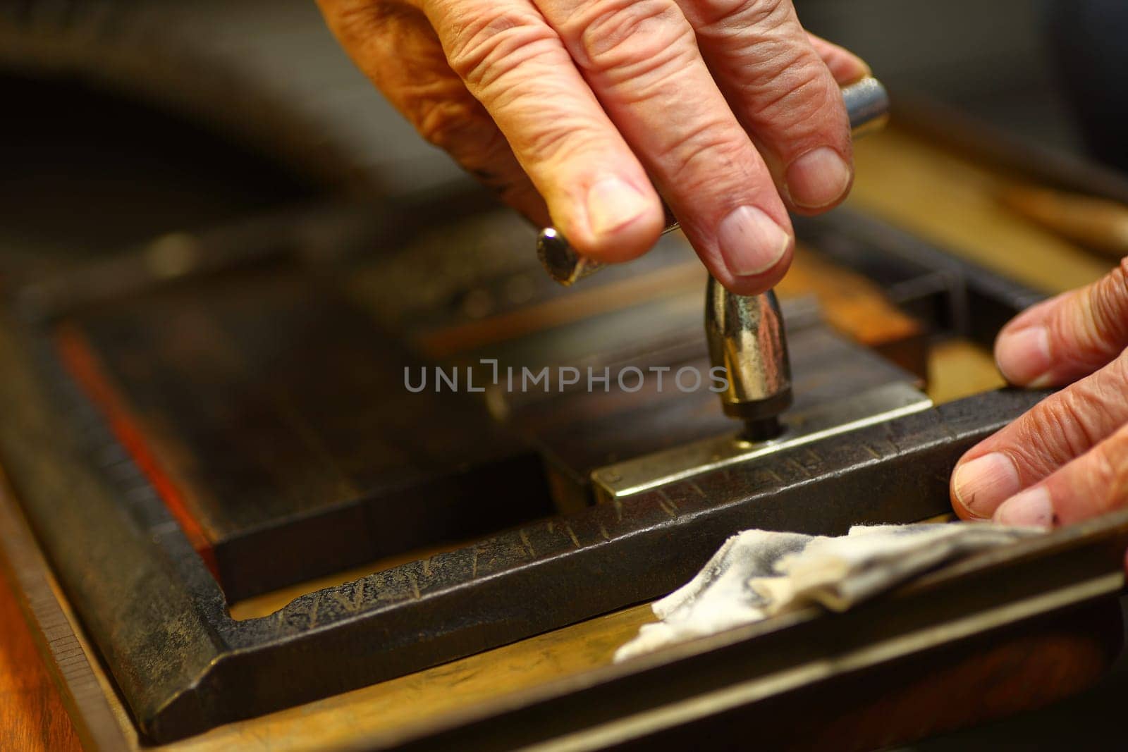 Closeup of ink-stained fingers of man using a quoin key to prepare type for letterpress printing.