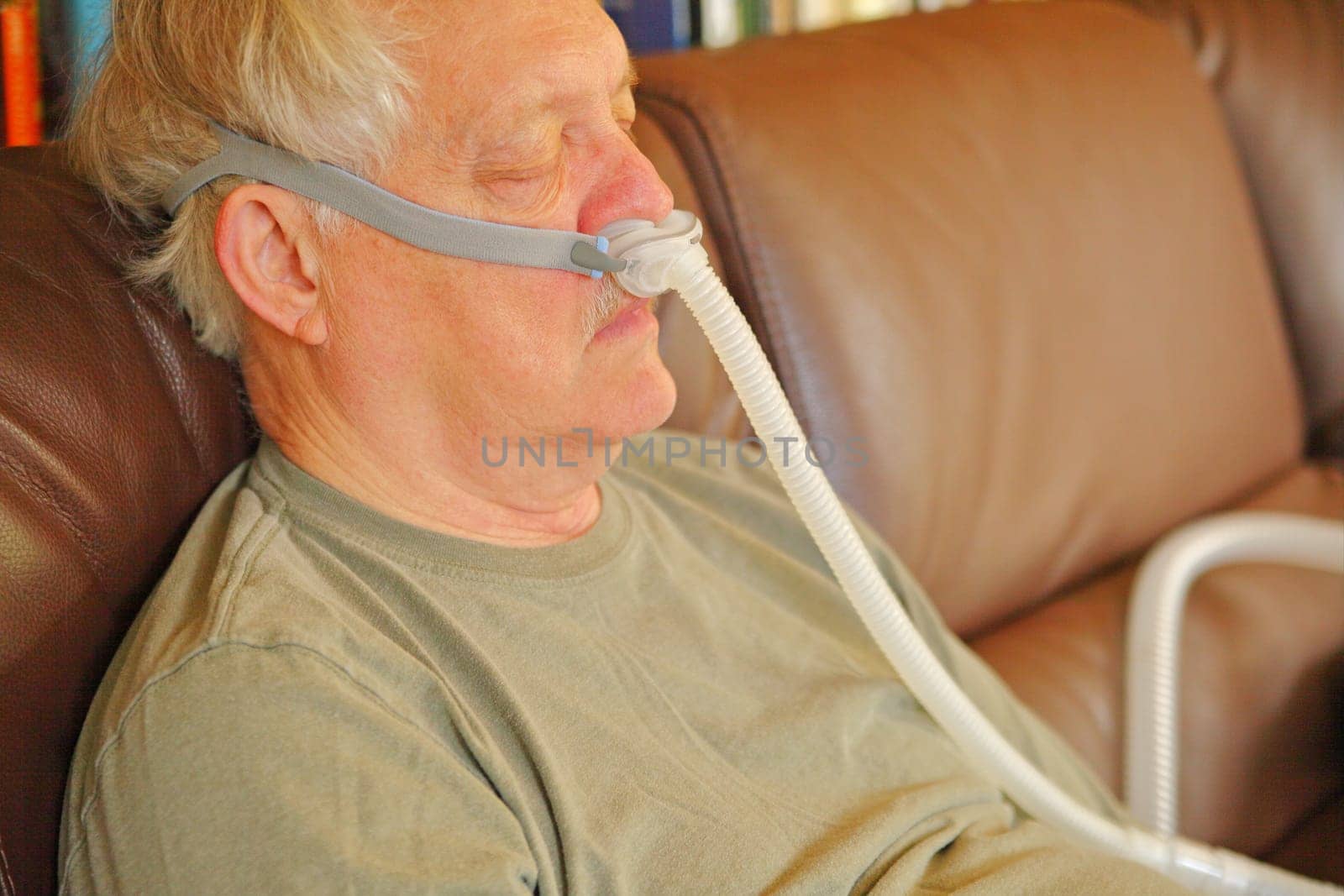 A man with sleep apnea rests on sofa, wearing a machine to help his breathing