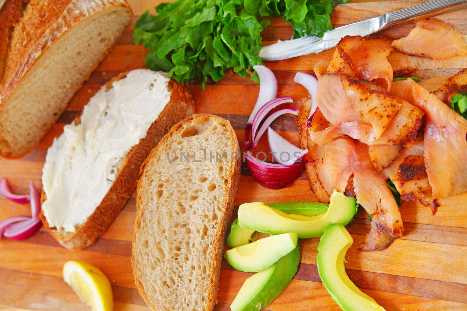 Overhead view of artisan bread slices, smoked salmon slices, avocado, red onion, lettuce and cream cheese