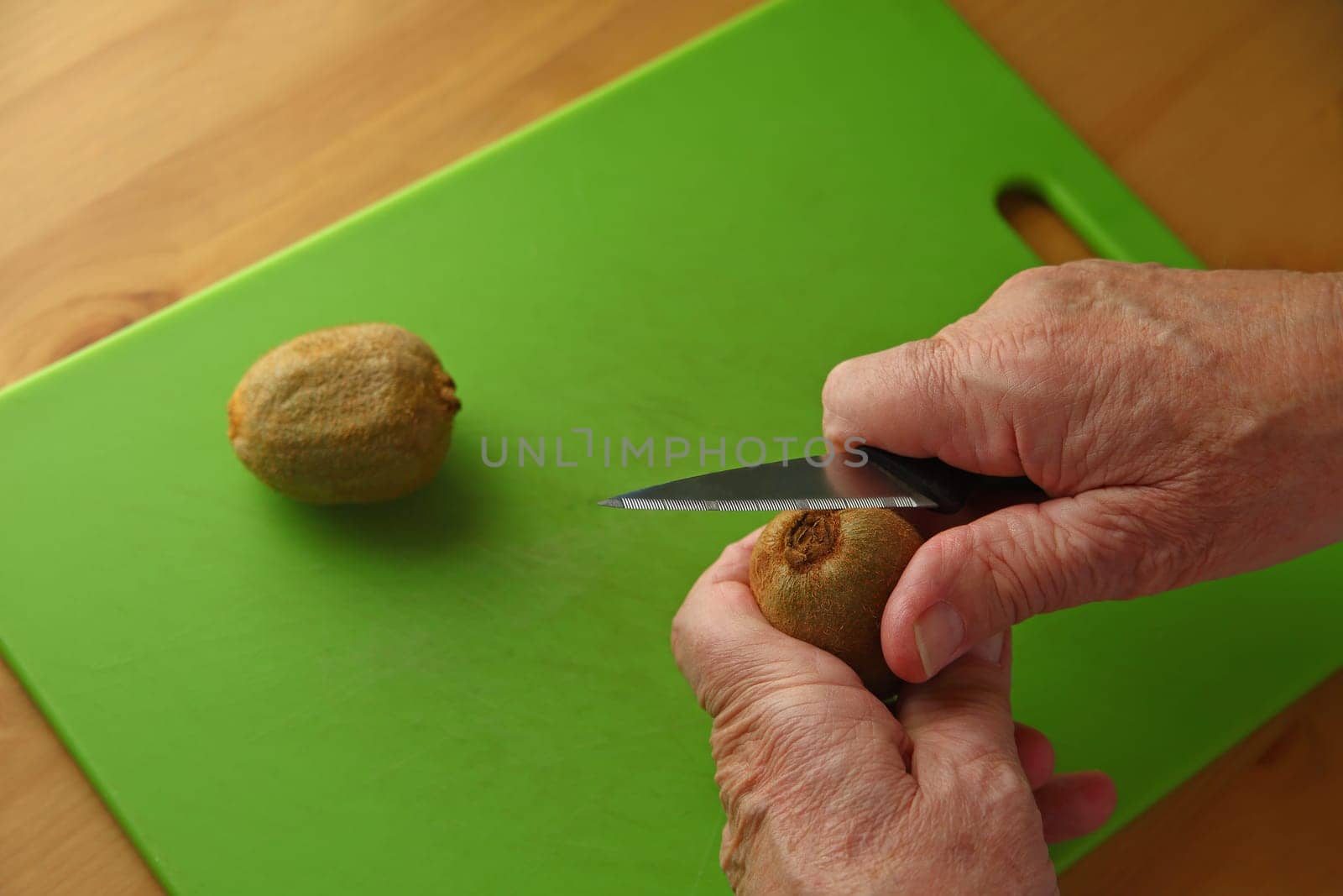 An older man peels a kiwifruit over a green cutting board