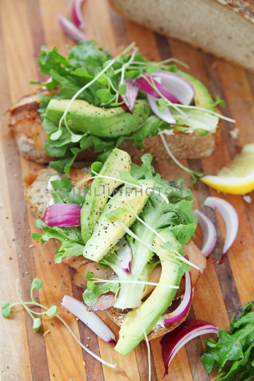 Vertical view of smoked salmon sandwiches with avocado, onions and sprouts on cutting board