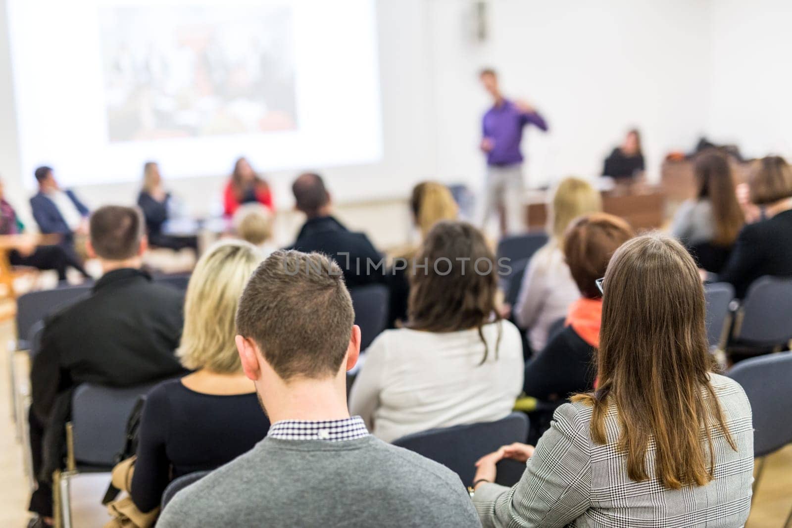 Business and entrepreneurship symposium. Speaker giving a talk at business meeting. Audience in the conference hall. Rear view of unrecognized participant in audience.