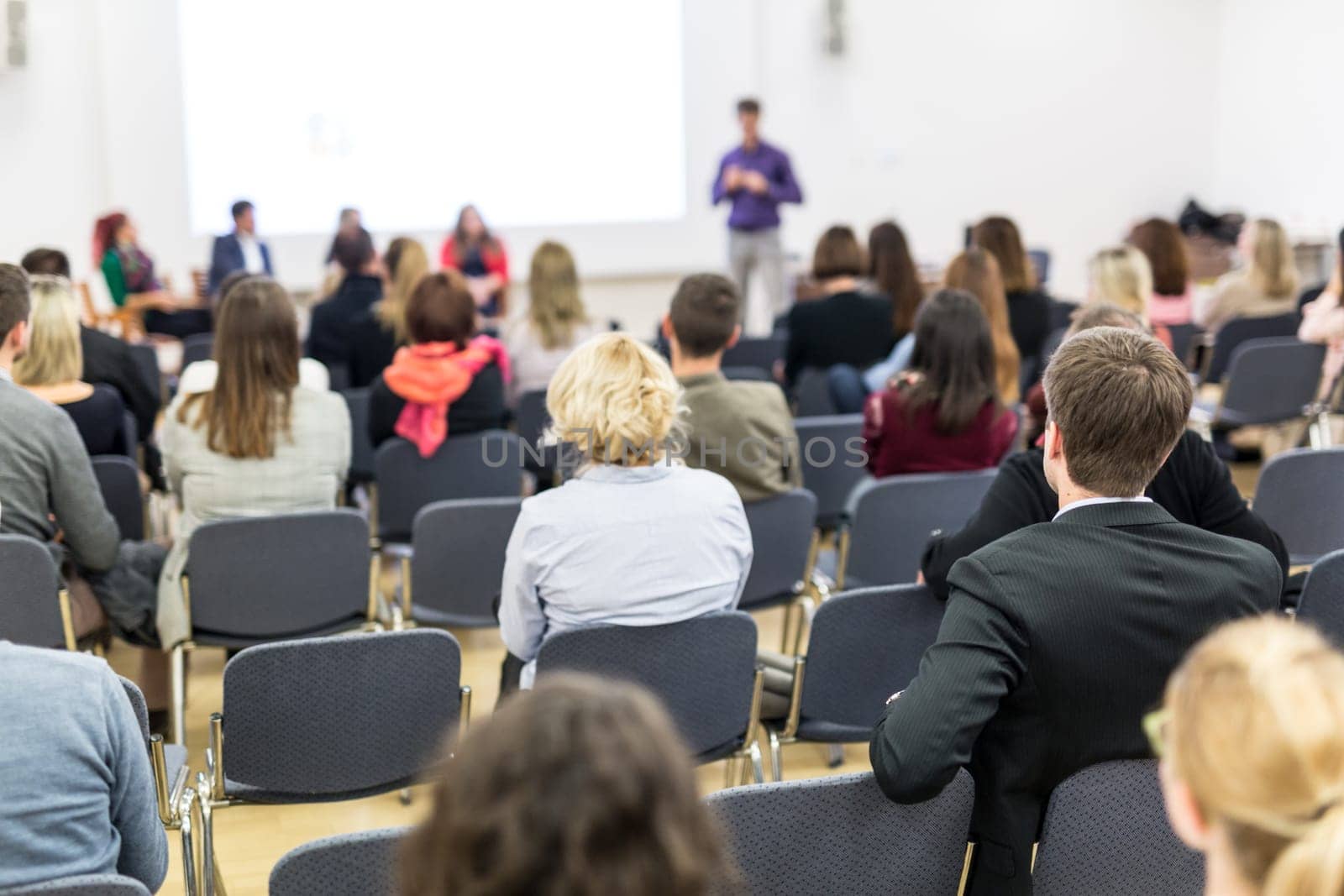 Business and entrepreneurship symposium. Speaker giving a talk at business meeting. Audience in the conference hall. Rear view of unrecognized participant in audience.
