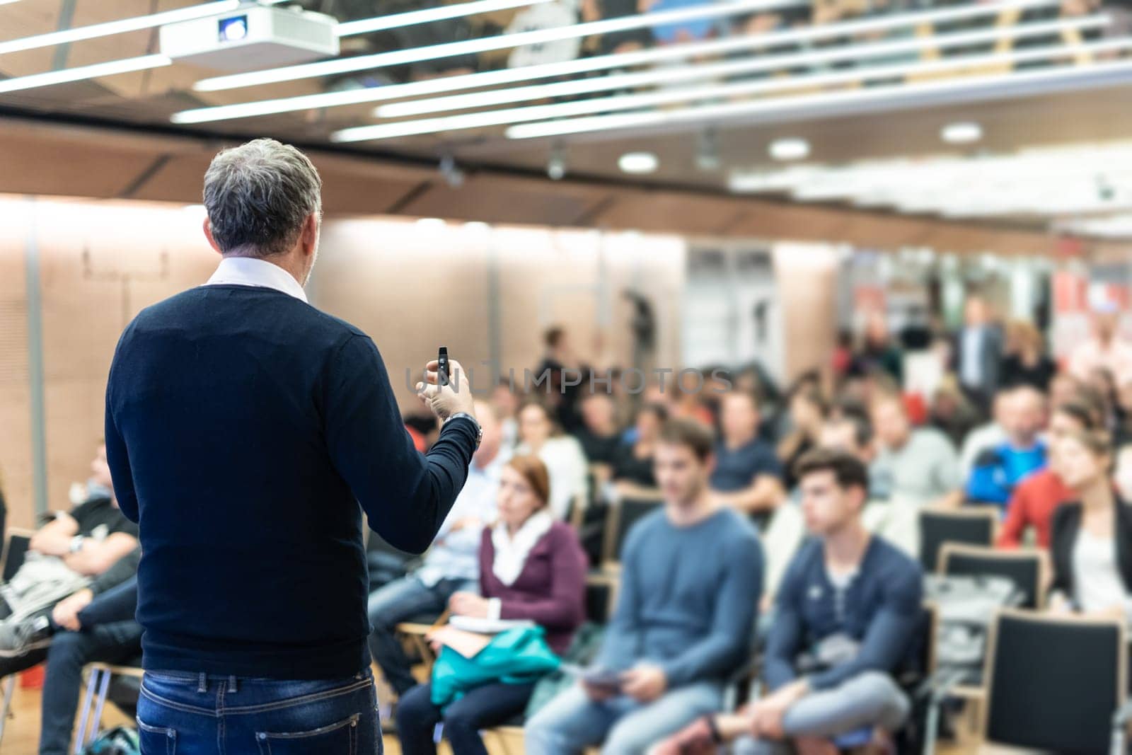 Expert giving a talk on business conference workshop. Unrecognizable people in audience at the conference hall. Business and entrepreneurship event.